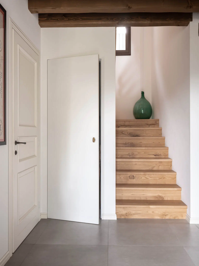 Un escalier moderne en bois clair. Une porte battante affleurante qui dissimule parfaitement le WC